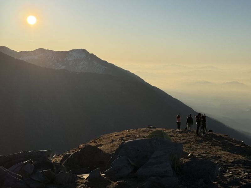 Group of trekkers standing on a sunlit ridge at Triund near Dharamkot, Himachal Pradesh Group of trekkers standing on a sunlit ridge at Triund near Dharamkot, Himachal Pradesh, with the Dhauladhar mountains in the background during golden hour sunrise