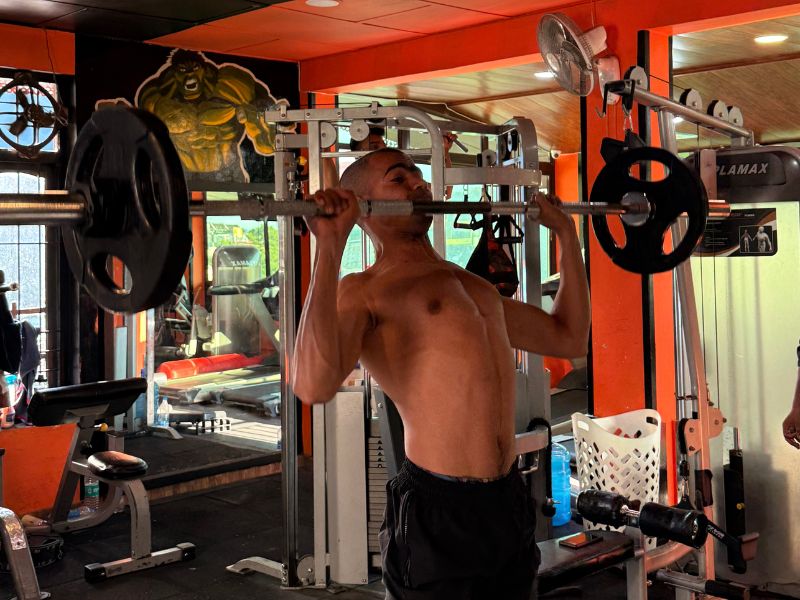Man performing standing barbell shoulder press in Dharamkot, focusing on strength training with weight plates on both sides of the bar